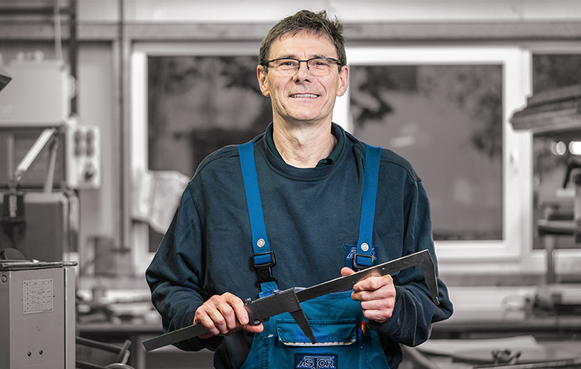 Employee in blue work clothes with glasses holds a tool in his hand and smiles.